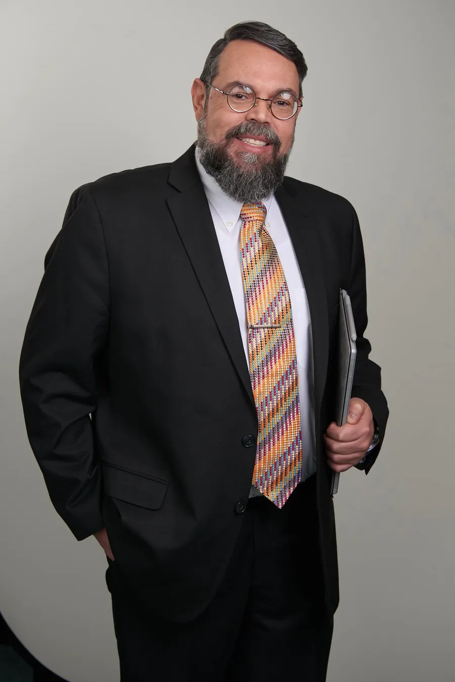 Studio portrait of Wilfredo in a dark suit and brightly patterned tie